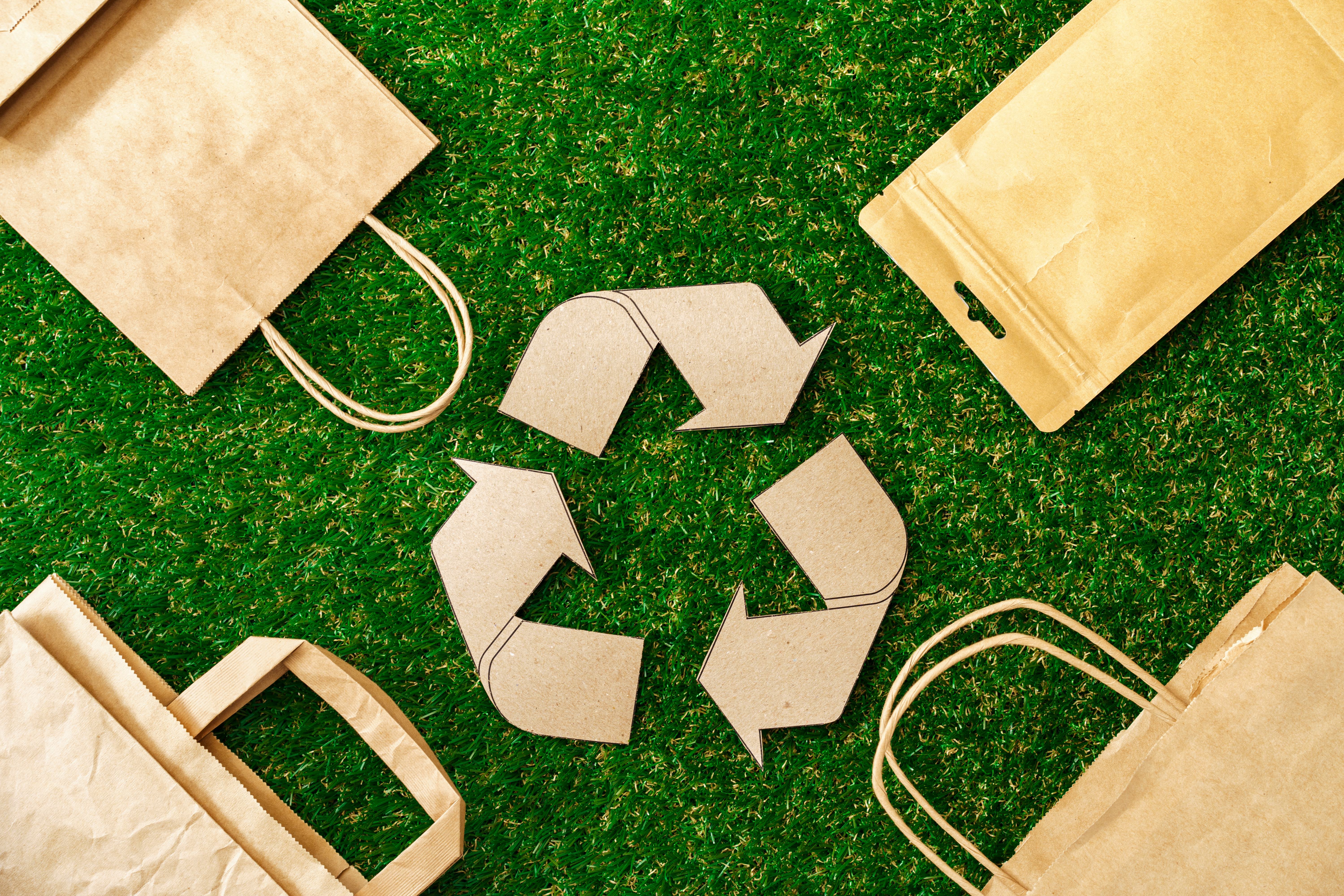 Recycle Sign with Paper Bags Around It On Green Grass