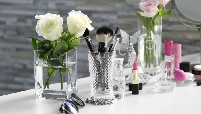 A collection of cosmetics arranged on a white vanity table with glass jars and roses.