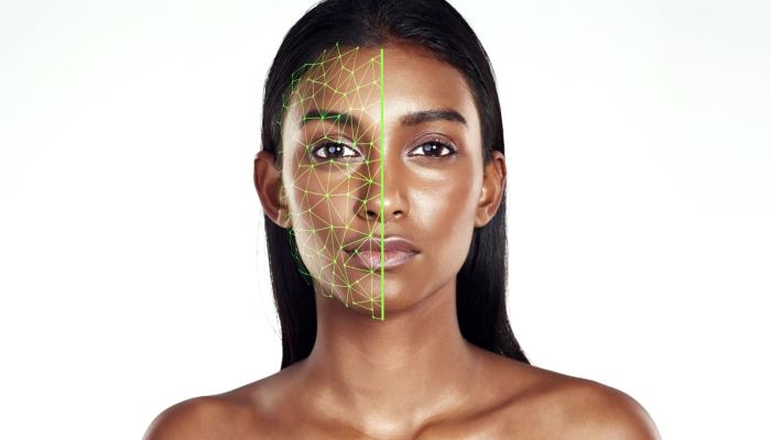 Studio portrait of a woman using facial recognition technology for skincare. The model is isolated against a white background, with a green hologram scanning the left side face to detect changes or enhancements.